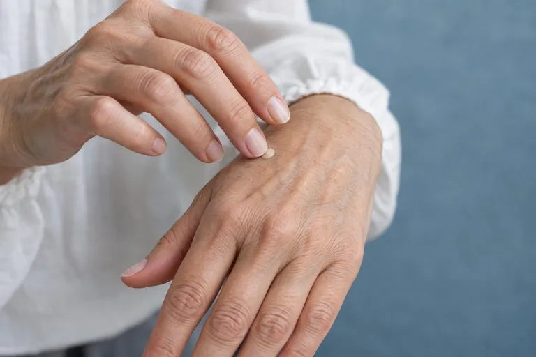 De ringvinger van een oudere hand tikt een klein stipje crème op de rug van de andere hand